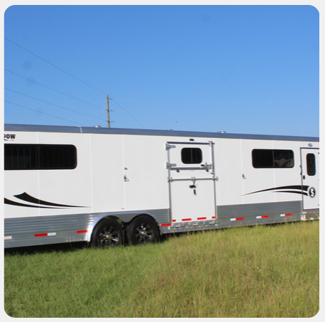 A horse trailer is parked in a grassy field