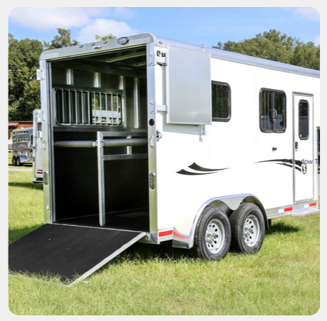 A white horse trailer is parked in a grassy field.