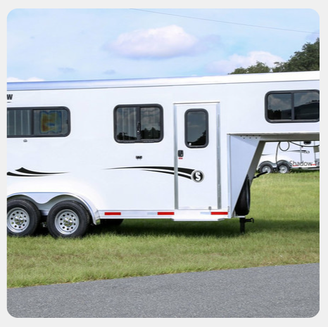 A white horse trailer is parked in a grassy field