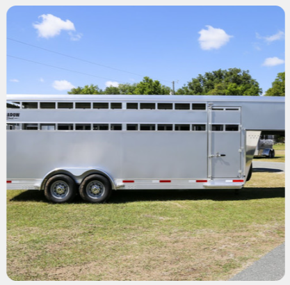 A silver horse trailer is parked in a grassy field