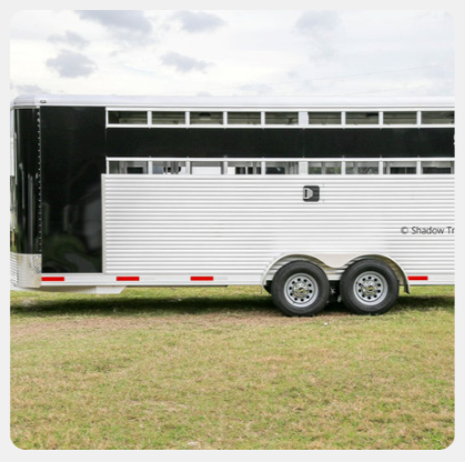 A white horse trailer is parked in a grassy field
