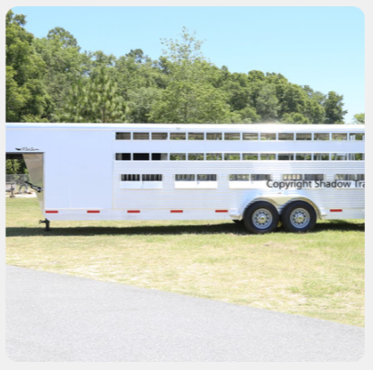 A white horse trailer is parked in a grassy field