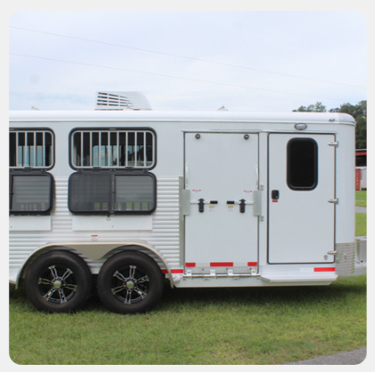 A white horse trailer is parked in a grassy field