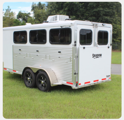 A shadow horse trailer is parked in the grass
