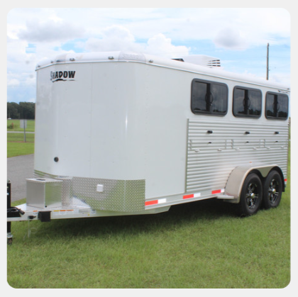 A white horse trailer is parked in a grassy field