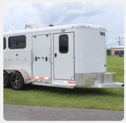 A white horse trailer is parked in a grassy field