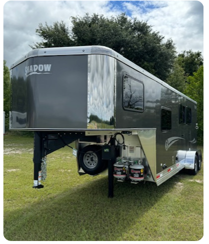 A horse trailer is parked in a grassy field.