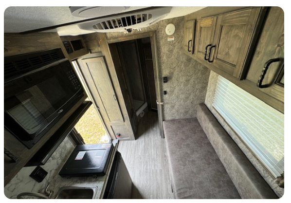 The inside of a camper with a microwave , sink , and cabinets.