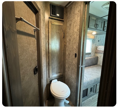 A bathroom in a rv with a toilet and a bed.