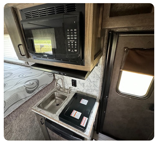 A kitchen in a rv with a sink , microwave , and stove.
