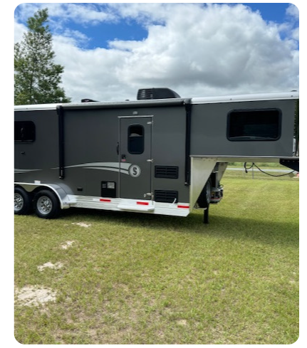 A horse trailer is parked in a grassy field.