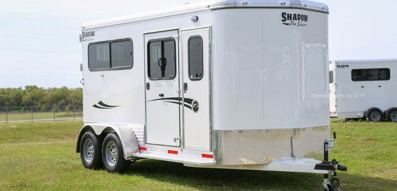 A white horse trailer is parked in a grassy field.