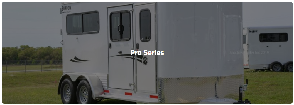 A white horse trailer is parked in a grassy field.