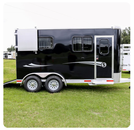 A black horse trailer is parked in a grassy field.