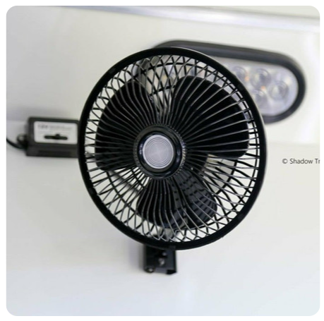 A black fan is sitting on a white surface next to a light