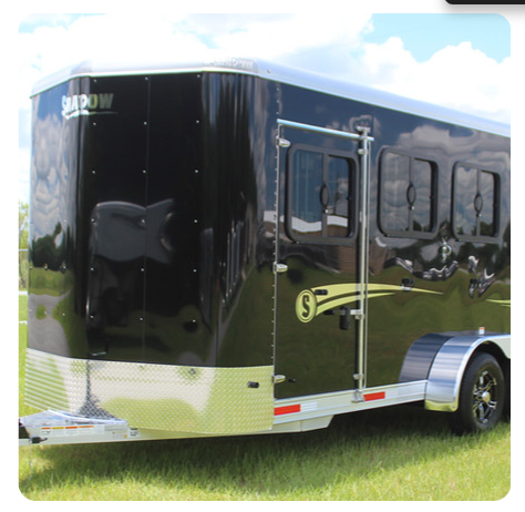 A black shadow trailer is parked in the grass