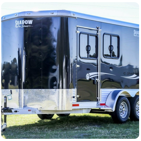 A black shadow trailer is parked in the grass