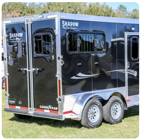 A black shadow trailer is parked in the grass