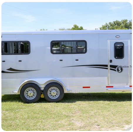 A white horse trailer is parked in a grassy field.