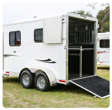 A white horse trailer is parked in a grassy field.