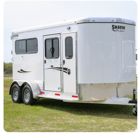 A white horse trailer is parked in a grassy field.