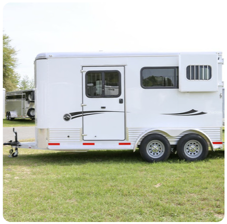 A white horse trailer is parked in a grassy field.