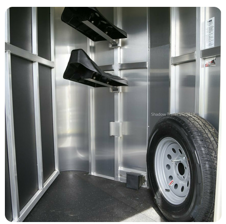 The inside of a horse trailer with a tire and saddle racks.
