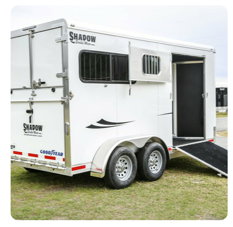 A white horse trailer is parked in the grass.