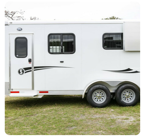 A white horse trailer is parked in a grassy field.