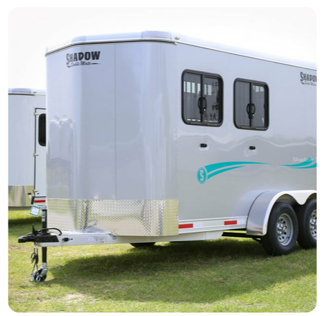 A horse trailer is parked in a grassy field.
