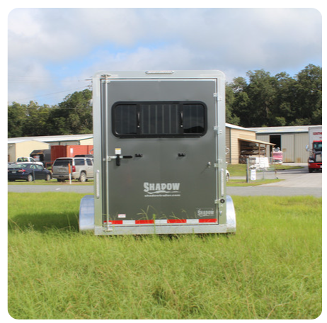 A horse trailer is parked in a grassy field.
