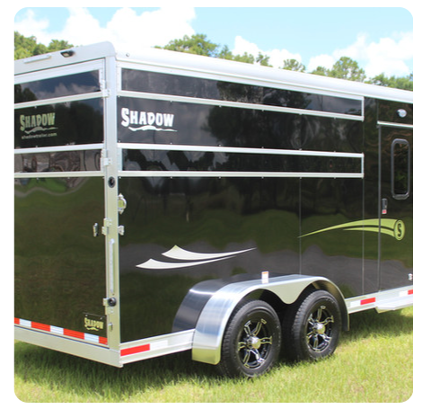 A black shadow trailer is parked in the grass
