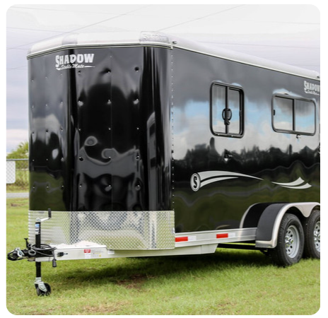 A black trailer is parked in a grassy field.