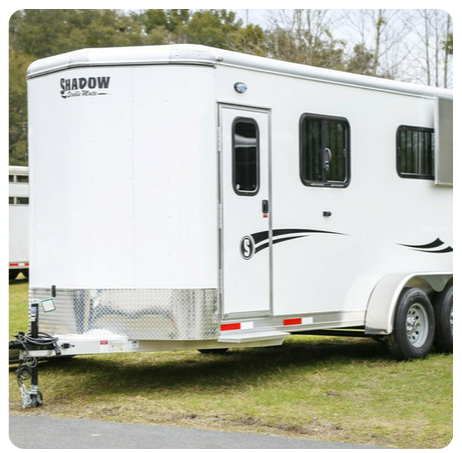 A white horse trailer is parked in a grassy field.