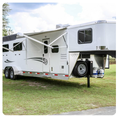 A white horse trailer is parked in a grassy field.