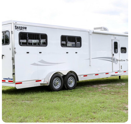 A white horse trailer is parked in a grassy field.