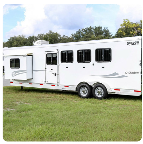 A white horse trailer is parked in a grassy field.