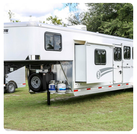 A white horse trailer is parked in a grassy field