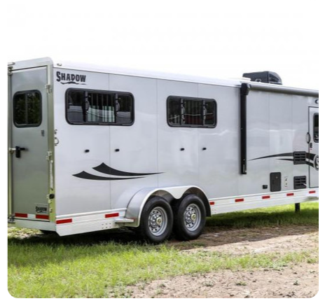 A white horse trailer is parked in a grassy field.