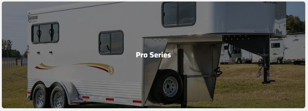 A white horse trailer is parked in a grassy field.