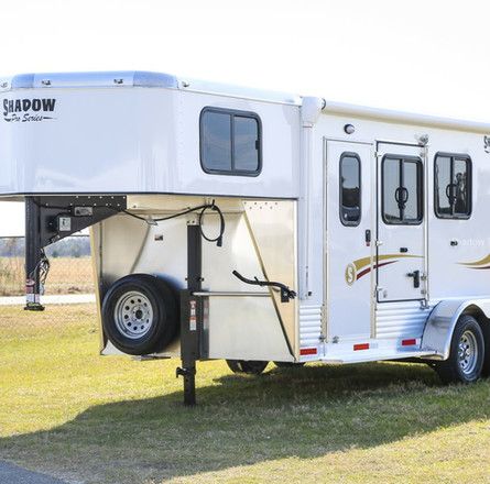 A white horse trailer is parked in a grassy field