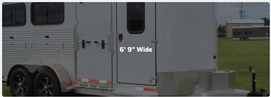 A white horse trailer is parked in a grassy field.