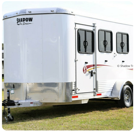 A white shadow trailer is parked in the grass