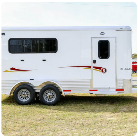 A white horse trailer is parked in a grassy field