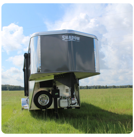 A shadow trailer is parked in a grassy field.