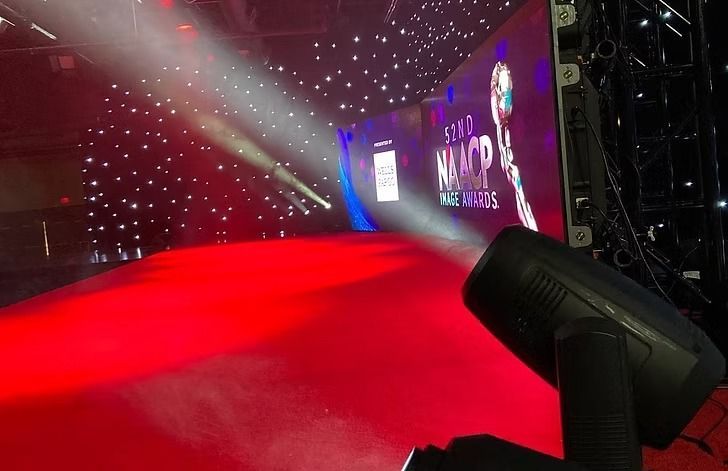 A red carpet runway with spotlights and a screen in the background, likely at an awards show.
