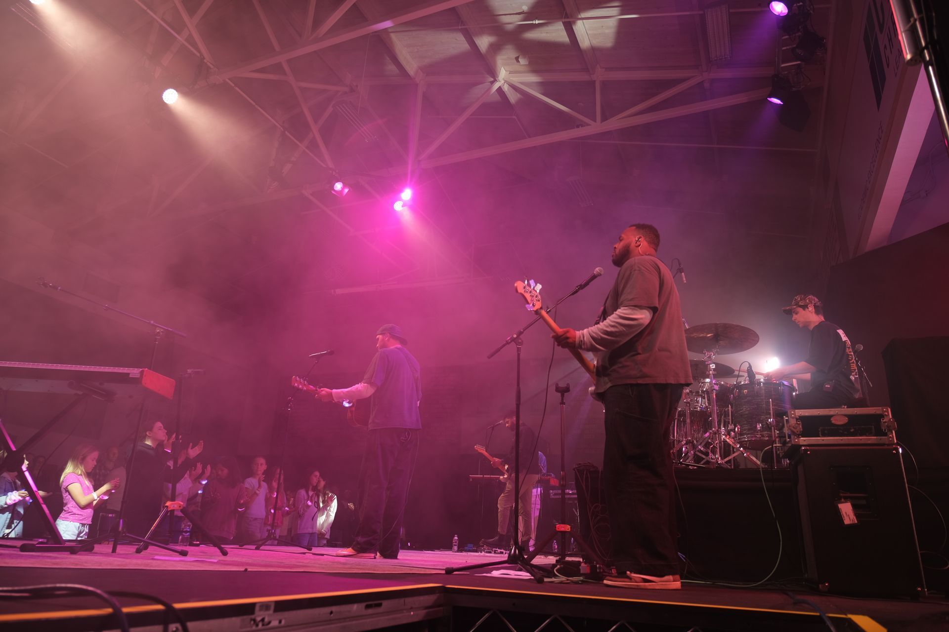 Band performing on stage under purple and white stage lights; audience visible.