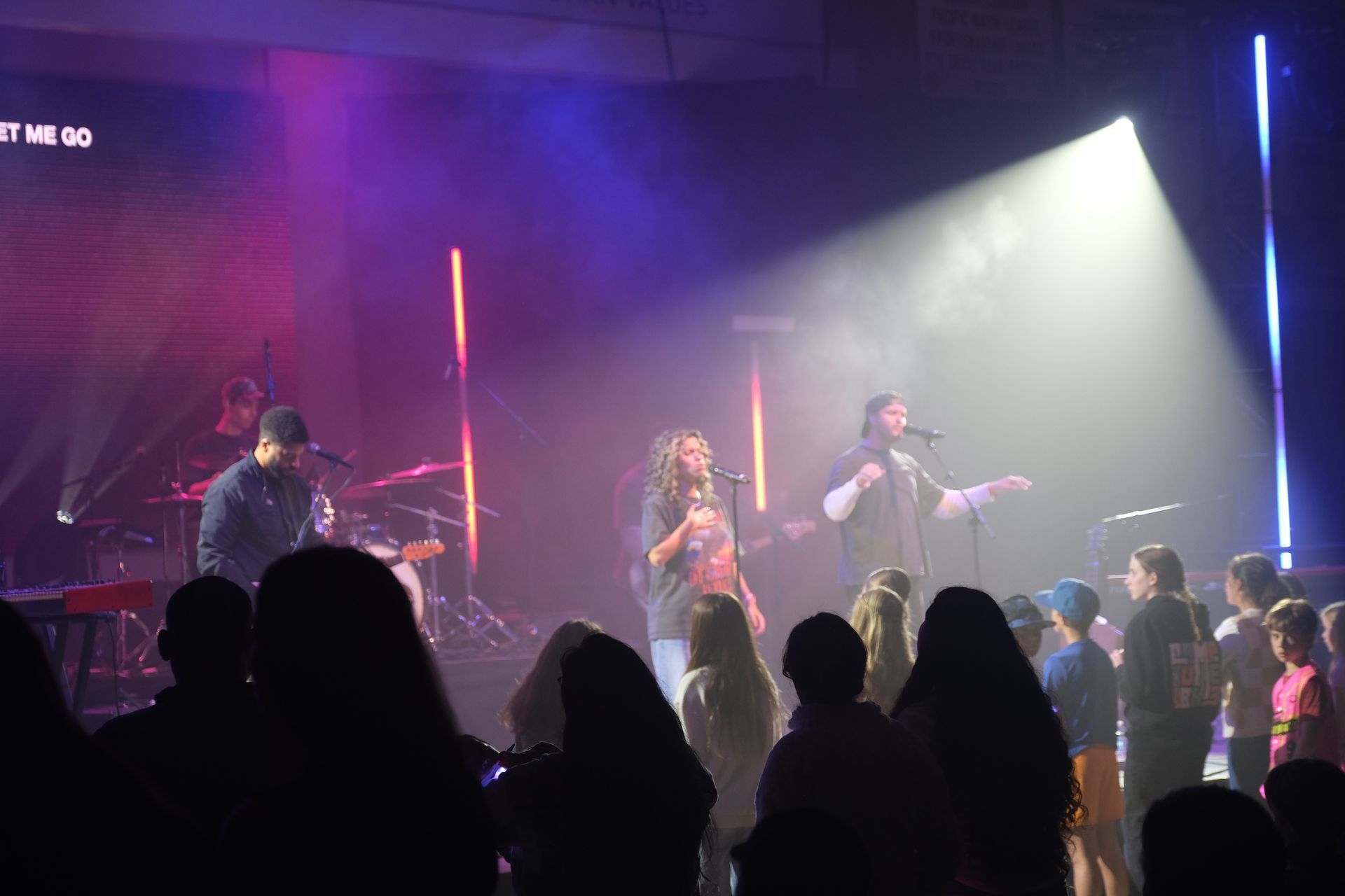Band performing on stage with audience. Purple and white stage lighting.
