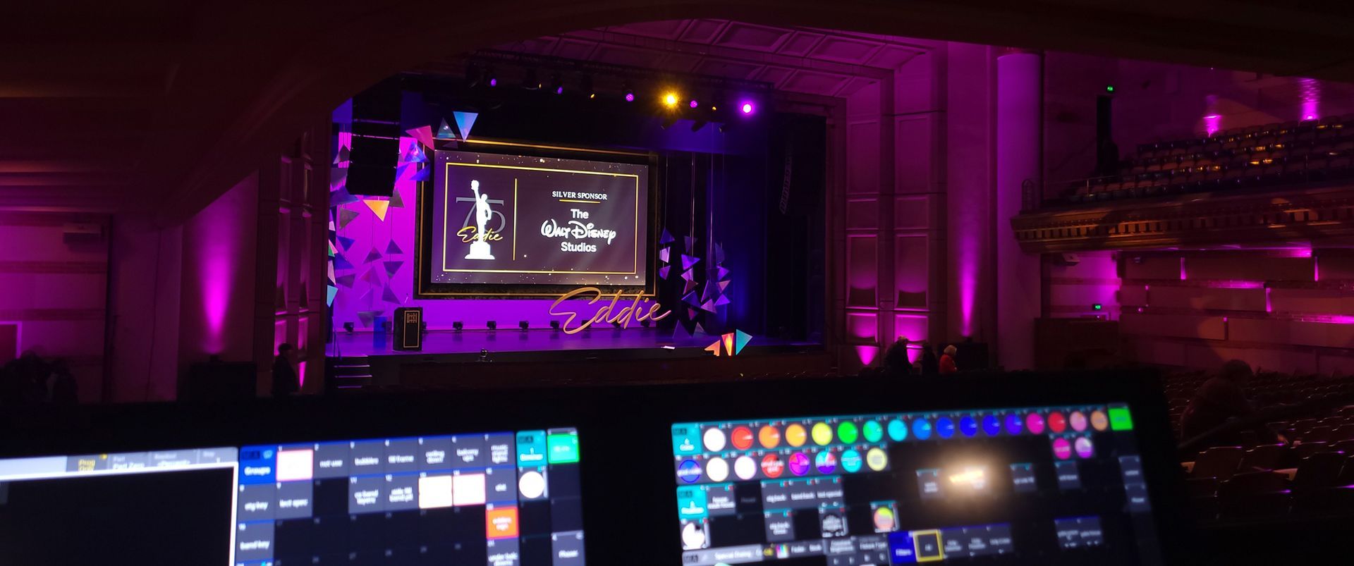 A stage bathed in purple light, with a control panel in the foreground. A screen displays an award's logo.
