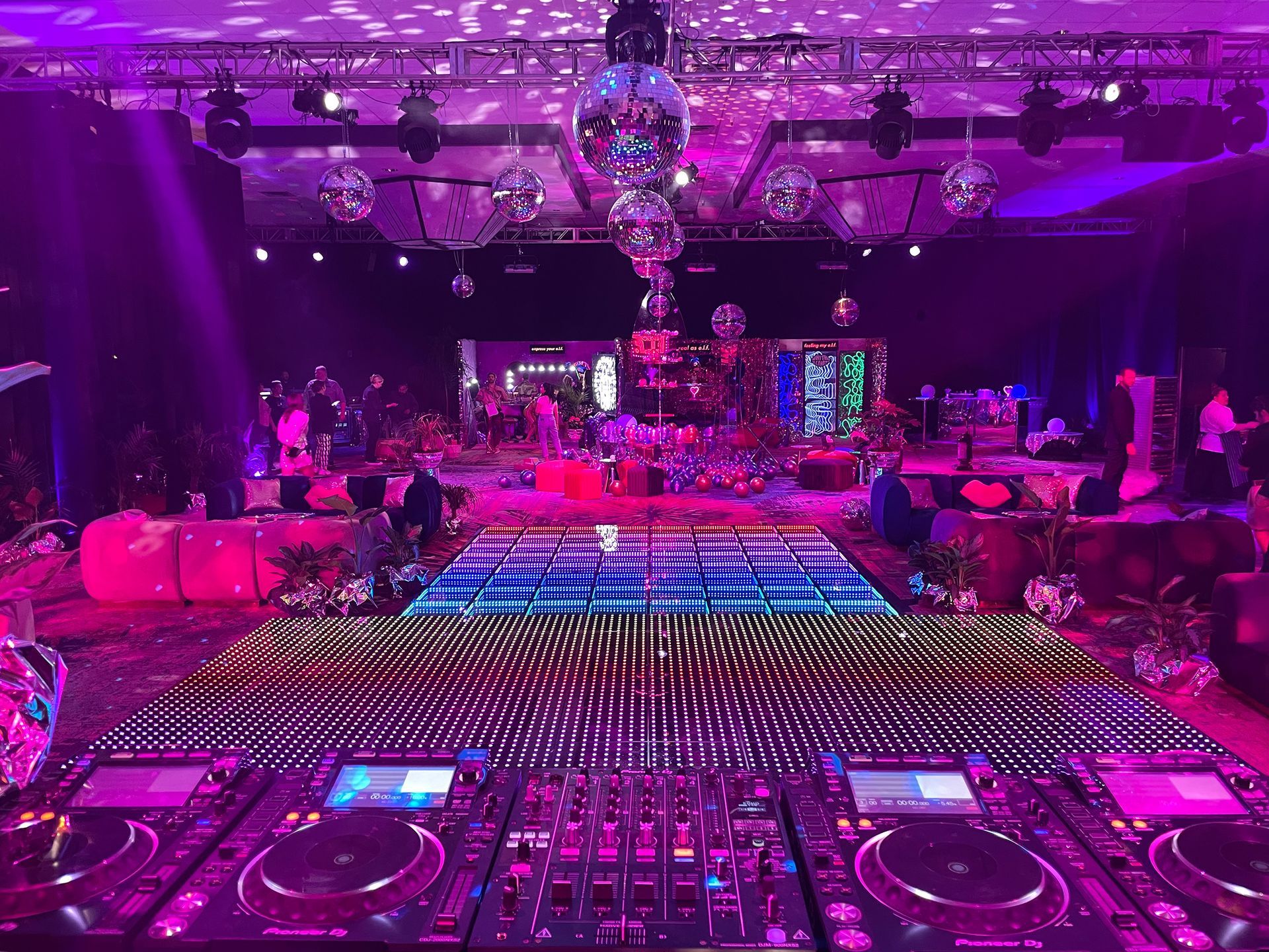 DJ setup at a party with a colorful dance floor, disco balls, and purple lighting.